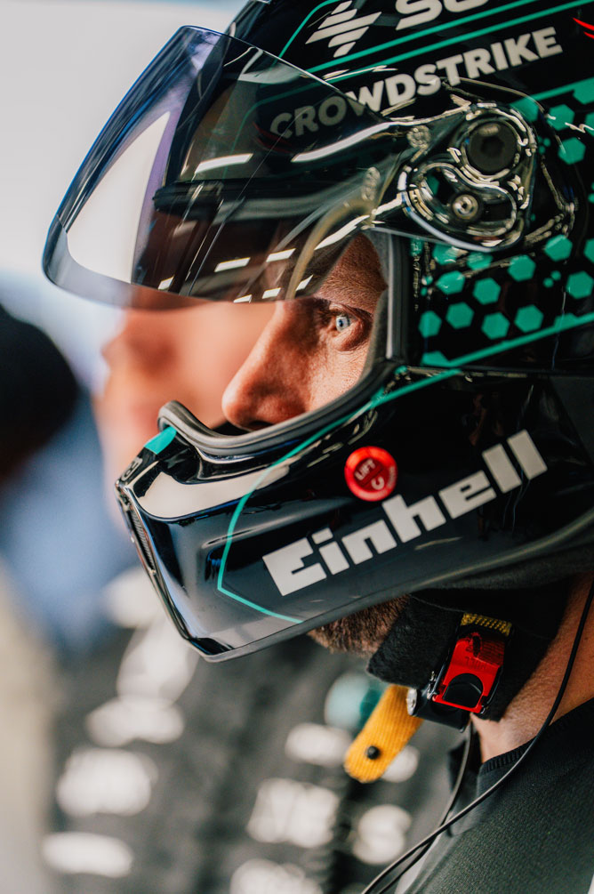 Član Formula 1 tima nosi kacigu i fokusirano gleda u stranu.