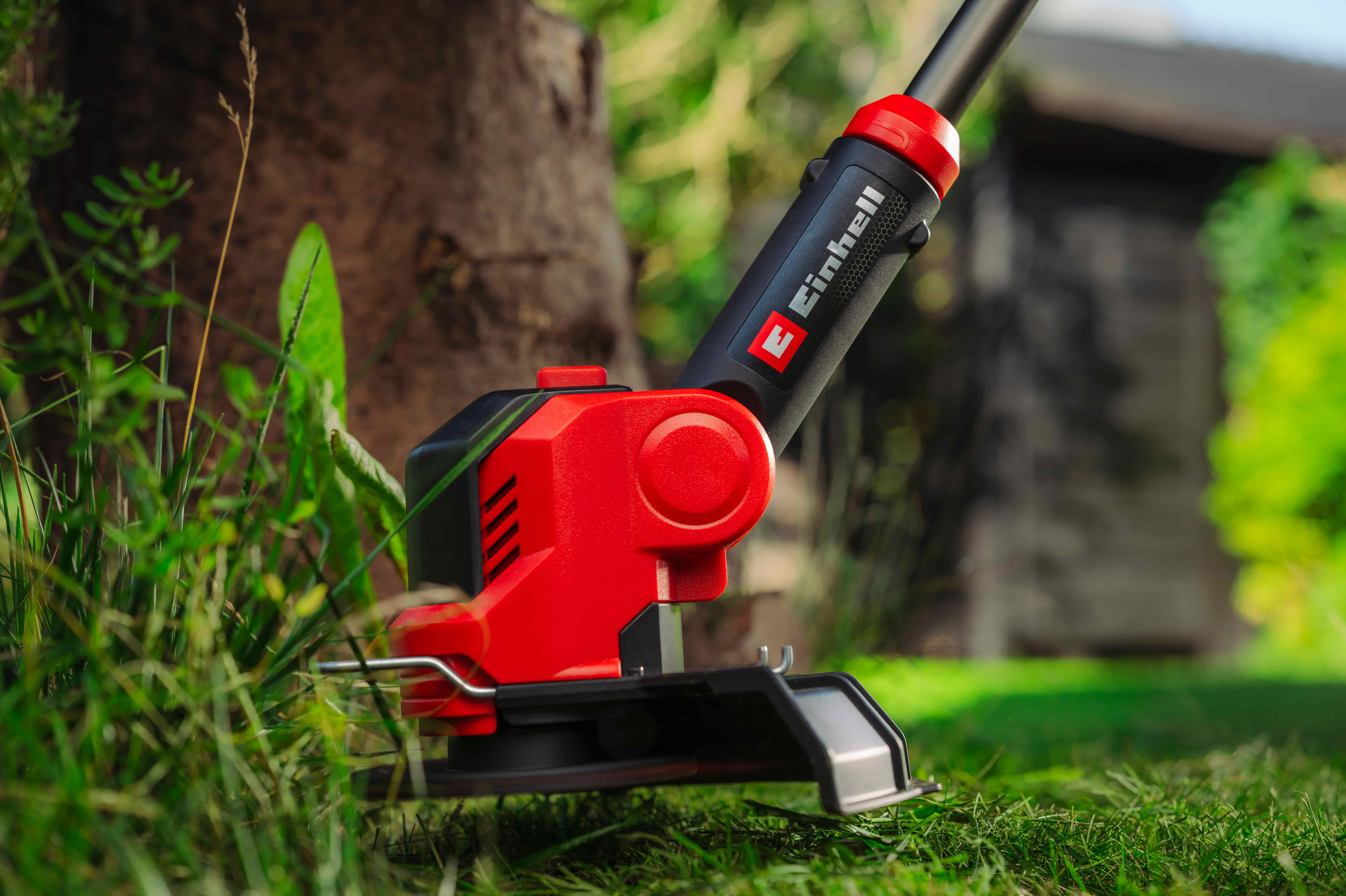 Einhell тример сече траву око дрвета у башти.