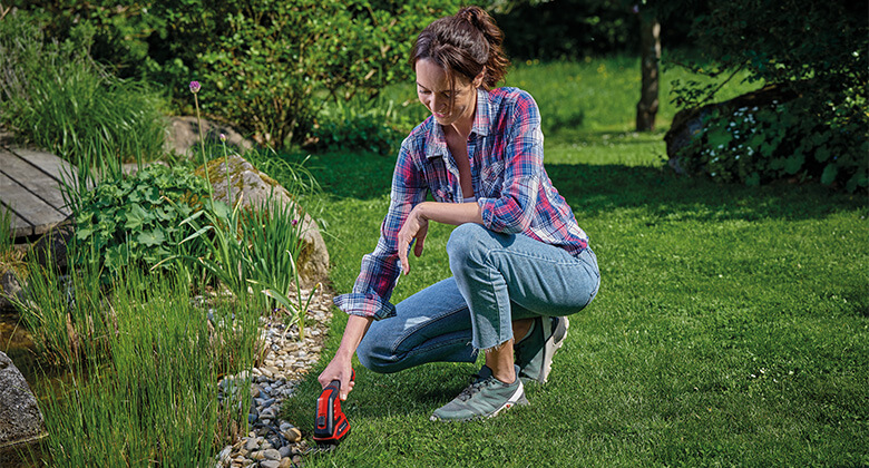 A woman cuts the grass at the edge of the lawn with Einhell grass shears.